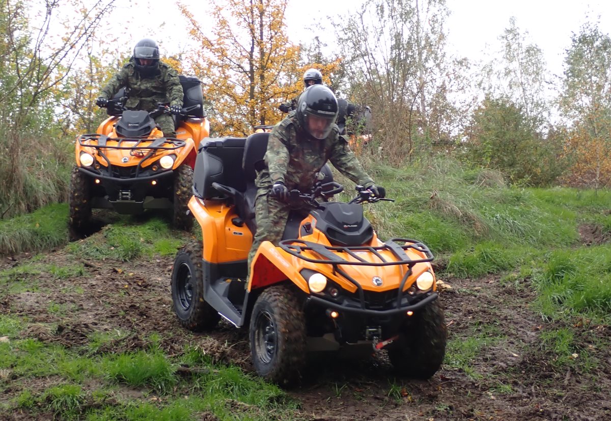 Trzech funkcjonariuszy Straży Granicznej na pojazdach ATV w terenie leśnym.