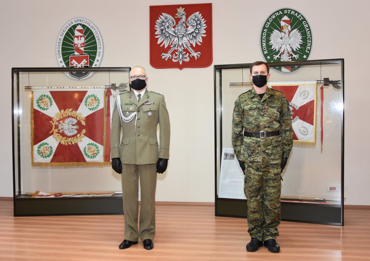 Komendant OSS SG w Lubaniu płk SG Jacek Wysokiński i nowo przyjęty do służby funkcjonariusz stoją na tle historycznych sztandarów