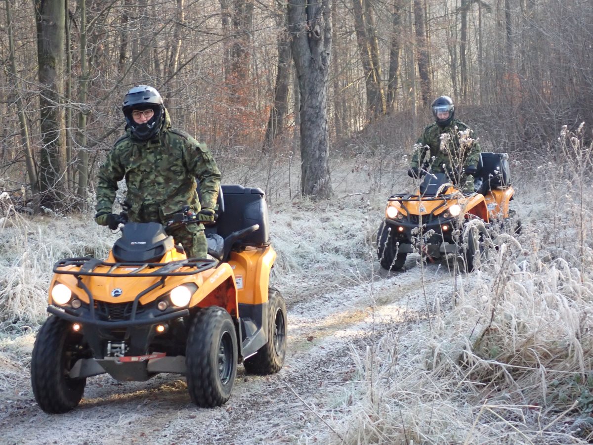 Dwóch funkcjonariuszy Straży Granicznej na pojazdach ATV w terenie leśnym.