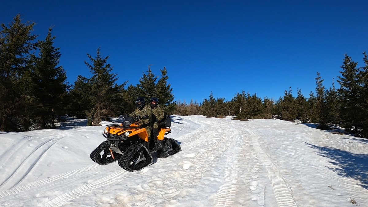 Funkcjonariusze Straży Granicznej na pojeździe ATV w terenie leśnym w scenerii zimowej..