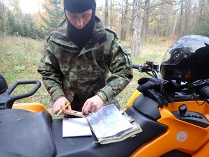  Funkcjonariusz Straży Granicznej w terenie leśnym stojący przed pojazdem ATV i przeglądający mapę.