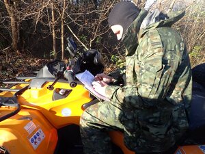 Funkcjonariusz Straży Granicznej na pojeździe ATV w terenie leśnym przeglądający mapę.