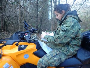  Funkcjonariuszka Straży Granicznej na pojeździe ATV w terenie leśnym przeglądająca mapę.