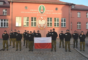 Grupa funkcjonariuszy Straży Granicznej z flagą polski na tle budynku