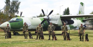 Zdjęcie grupowe przewodników z psami służbowymi. W tle samolot