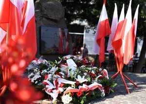 Flagi Państwowe oraz kwiaty złożone przed pomnikiem