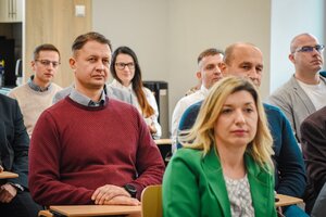 Uczestnicy spotkania siedzący na krzesłach w sali wykładowej