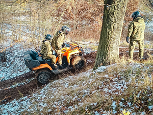 Dwóch funkcjonariusz SG siedzący w żółtym pojeździe typu ATV, pojdjeżdzający pod górkę, obok drzewa tyłem stoi funkcjonariusz, SG podczas zajęć w lesie Dwóch funkcjonariusz SG siedzący w żółtym pojeździe typu ATV, pojdjeżdzający pod górkę, obok drzewa tyłem stoi funkcjonariusz, SG podczas zajęć w lesie