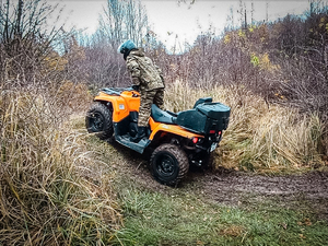 Funkcjonariusz SG siedzący w żółtym pojeździe typu ATV, pojdjeżdzający pod górkę podczas zajęć w lesie Funkcjonariusz SG siedzący w żółtym pojeździe typu ATV, pojdjeżdzający pod górkę podczas zajęć w lesie