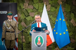 Starosta Powiatu Lubańskiego stojący przy mównicy, w tle flaga Polski i UE