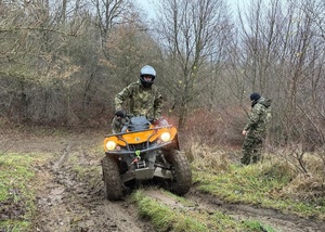 Funkcjonariusz SG na pojeździe ATV podczas szkolenia w terenie. W tle instruktor prowadzący szkolenie Funkcjonariusz SG na pojeździe ATV podczas szkolenia w terenie. W tle instruktor prowadzący szkolenie