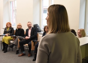 Warsztaty nt. Traumy Wojennej Na pierwszym planie prowadząca warsztaty. W tle na krzesłach siedzą uczestnicy warsztatów