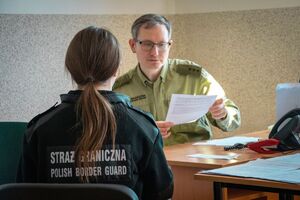 Kursantka szkolenia w zakresie szkoły podoficerskiej podczas egzaminu Kursantka szkolenia w zakresie szkoły podoficerskiej siedząca tyłem przy stole,przed nią Funkcjonariusz SG z komisji egzaminacyjnej