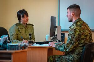 Kursant szkolenia w zakresie szkoły podoficerskiej podczas egzaminu Kursant szkolenia w zakresie szkoły podoficerskiej siedzący przy biurku, z drugiej strony Funkcjonariuszka SG z komisji egazminacyjnej