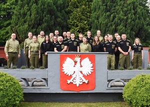 Kurs doskonalący pt. „Postępowanie w sprawie zobowiązania cudzoziemca do powrotu” Grupa funkcjonariuszy SG na trybunie ośrodka. Na trybunie znajduje się godło RP